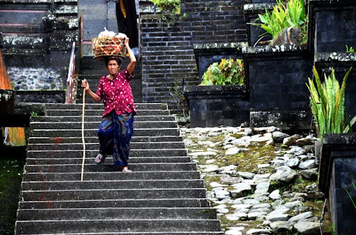 an old lady step down a stairs while carrying a big basket on her head