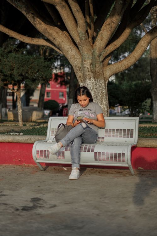 Free A young woman sitting on a park bench, enjoying a relaxing moment outdoors. Stock Photo