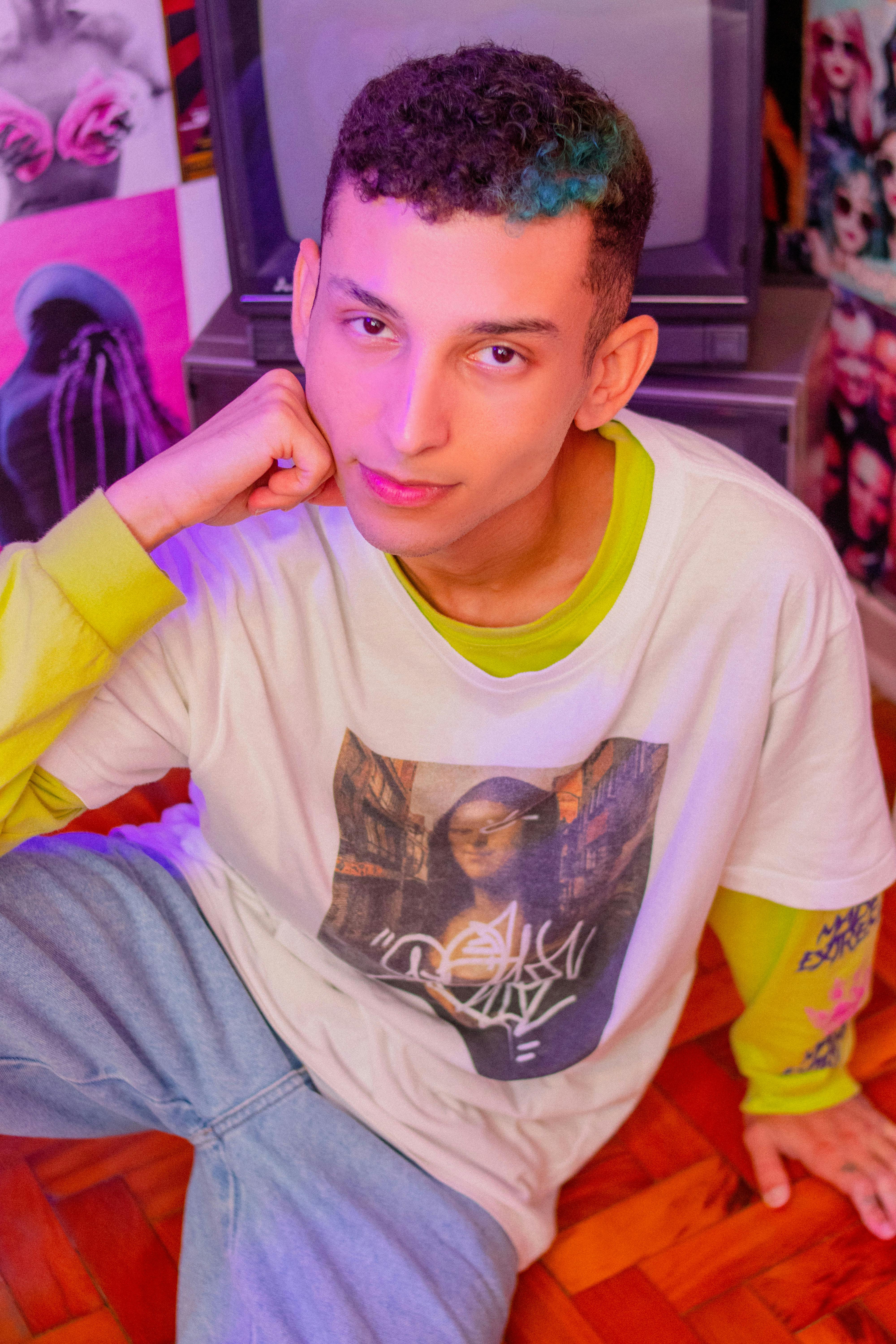 Stylish young man in casual wear sitting indoors, striking a pose with a retro-inspired setting.