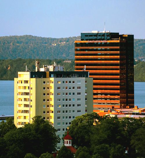 Free Aerial view of modern buildings near a lake surrounded by lush hills under a blue sky. Stock Photo