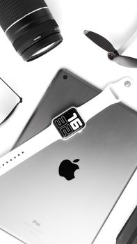 Minimalist flat lay of tech gadgets including a smartwatch, tablet, and camera lens on a desk.