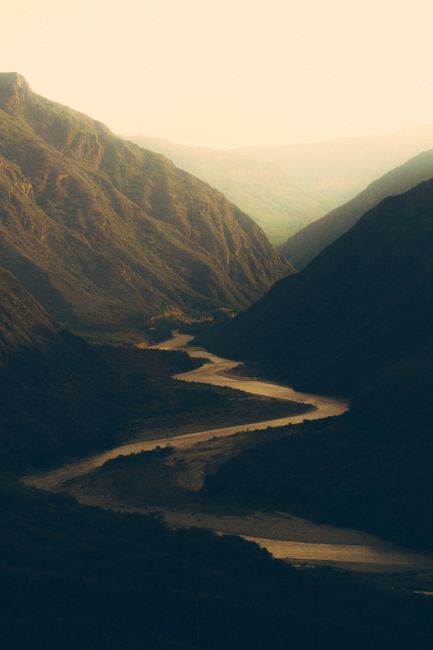 Captivating landscape of a winding river flowing through a valley between majestic mountains at dusk.