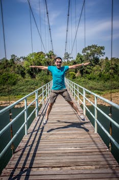 一个快乐的男人在郁郁葱葱的森林背景下跳上了木制吊桥