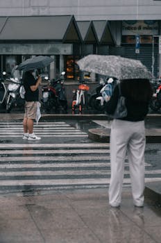 People with umbrellas crossing a wet street in the rain, showcasing a typical rainy day.