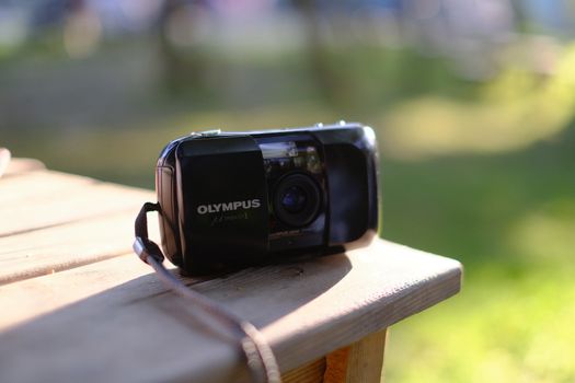 Stylish retro Olympus analog camera resting on a sunlit wooden table outdoors.