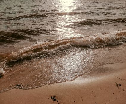Peaceful view of waves crashing on a sandy beach during sunset, reflecting golden light.