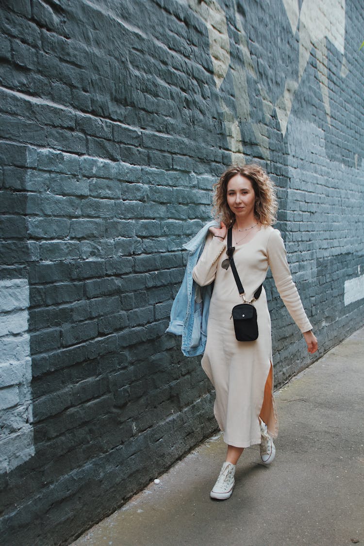 Woman In Beige Long Sleeves Dress Walking On The Street Side While Looking At The Camera