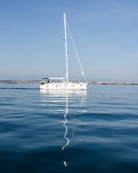 A tranquil scene of a sailboat sailing in calm waters, reflecting clear skies.