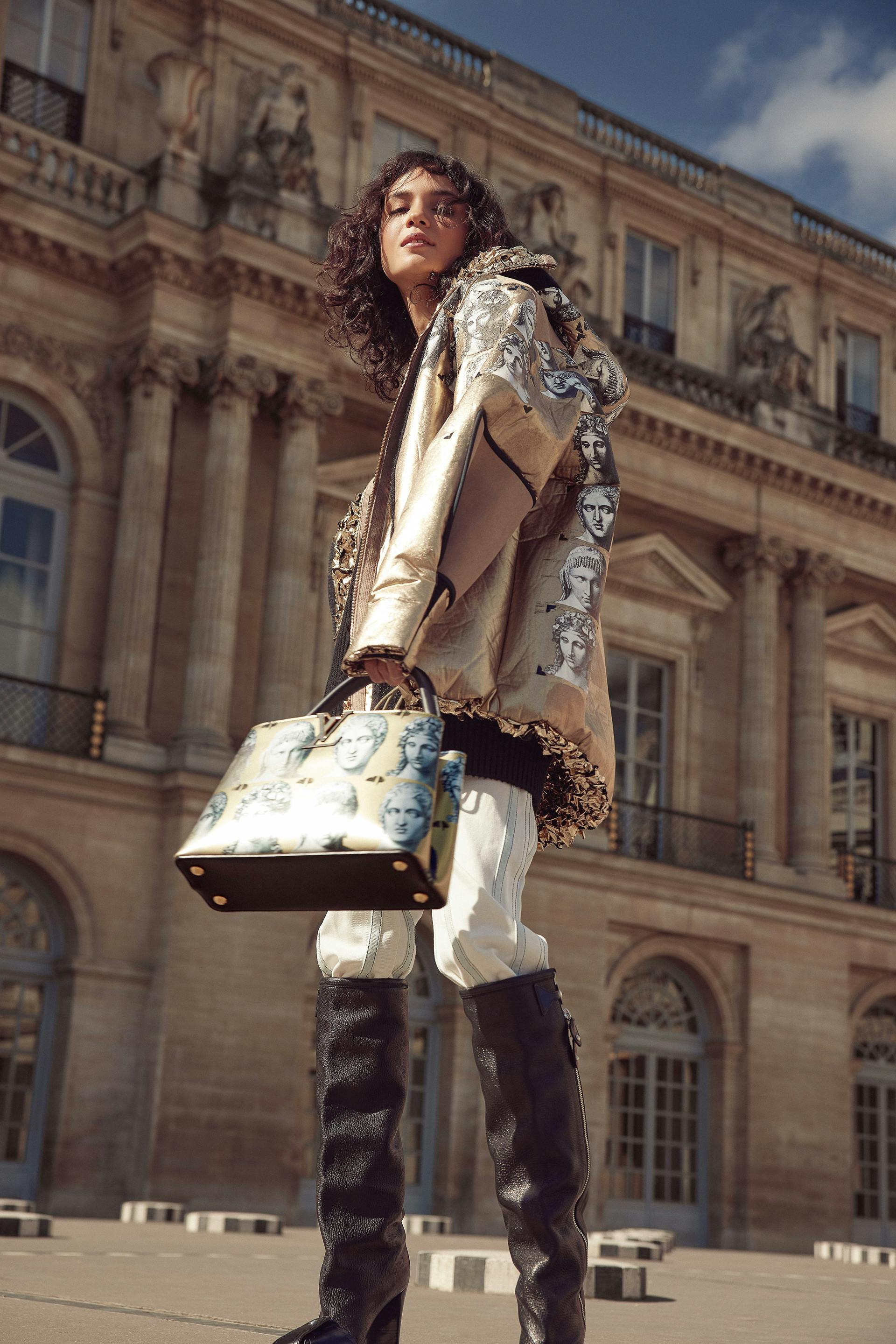 Stylish woman posing outdoors with a designer bag and jacket, architectural background.