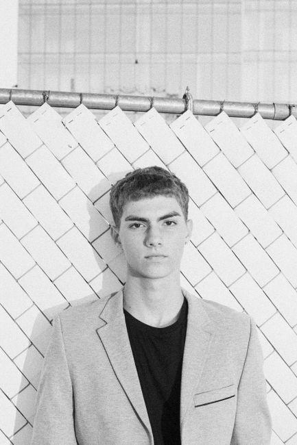 Black and white portrait of a young man wearing a jacket, showing a modern fashion style.