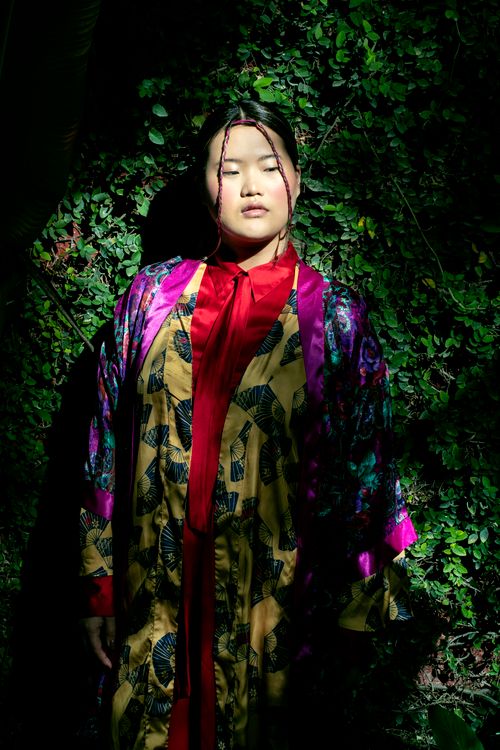 Free A young woman stands against lush greenery, wearing a colorful traditional dress. Stock Photo