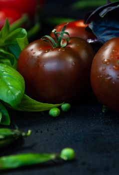 Close-up of wet tomatoes and basil leaves on a dark background, showcasing fresh produce.