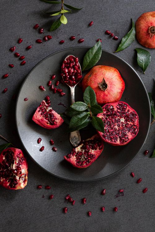 Free Top view of pomegranates with leaves on a dark plate, showcasing vibrant seeds. Stock Photo