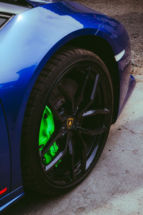 Free Detailed view of a Lamborghini wheel showcasing a vibrant green brake caliper against a blue car body. Stock Photo