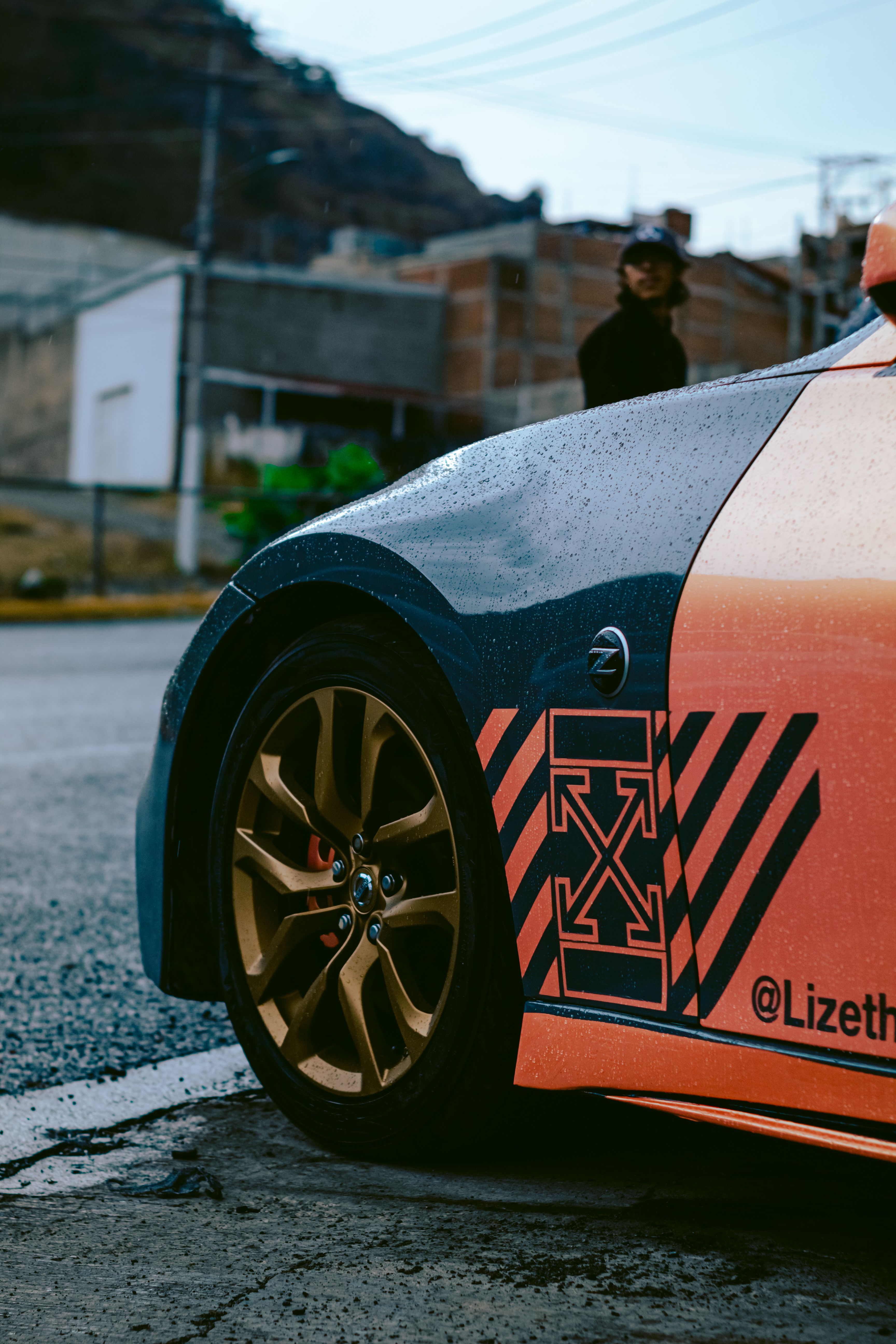 Custom Nissan 370Z close-up showcases unique paint design and rims, captured on a rainy day.