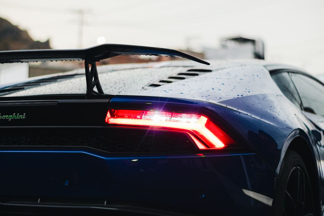 close up of a blue lamborghini showing rear light and water droplets o