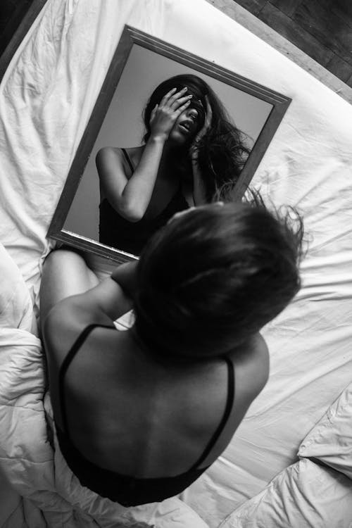 Woman Sitting on Bed Staring at Reflection in Mirror