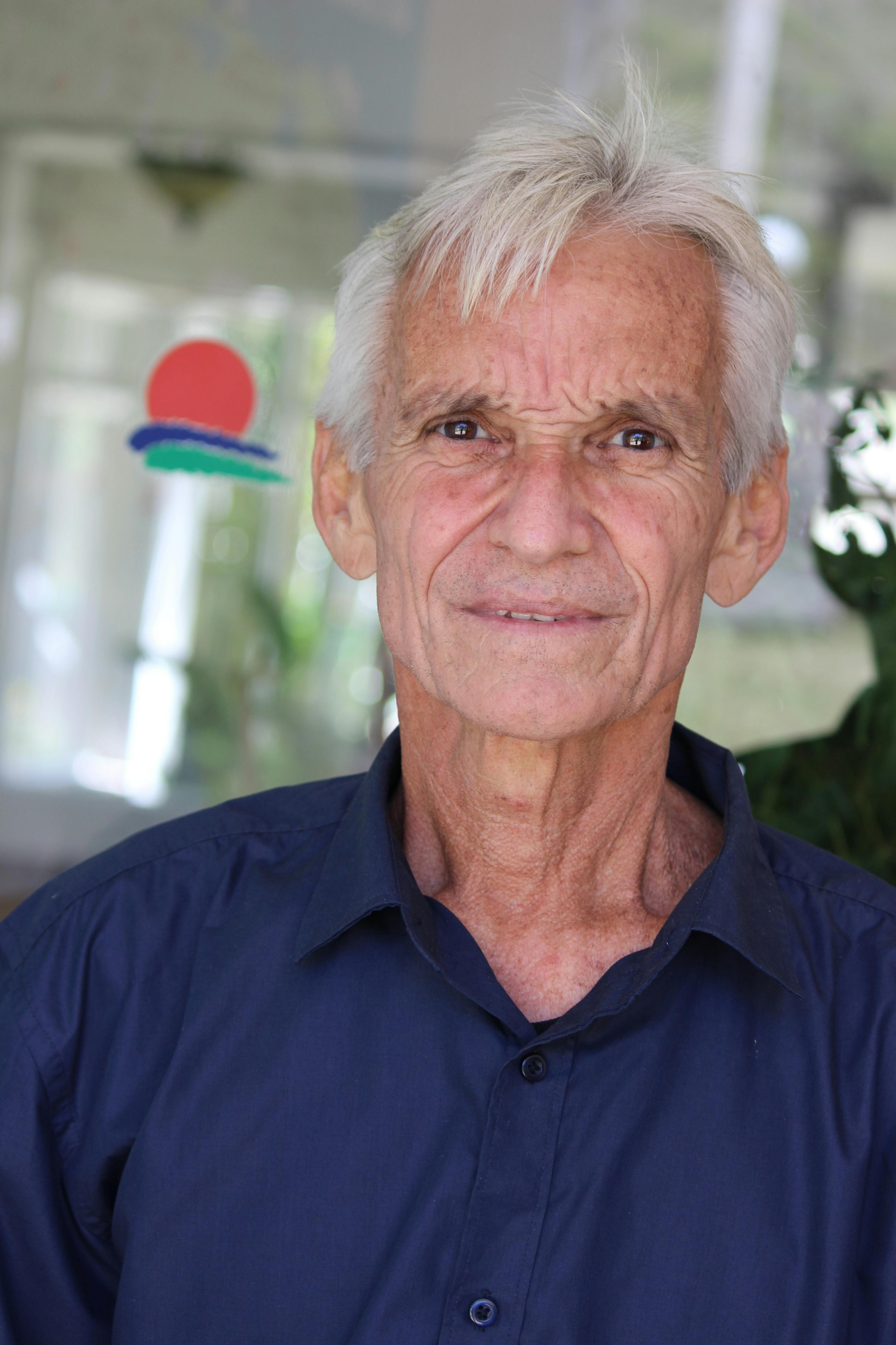 Portrait of a senior man with white hair, wearing a blue shirt, indoors.