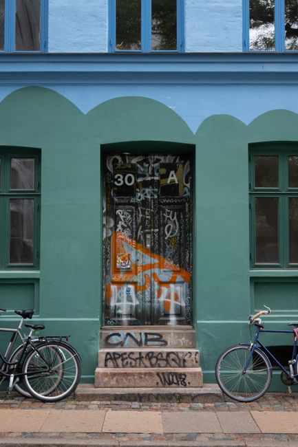 Vibrant urban scene of a graffiti-covered doorway flanked by bicycles in Copenhagen.