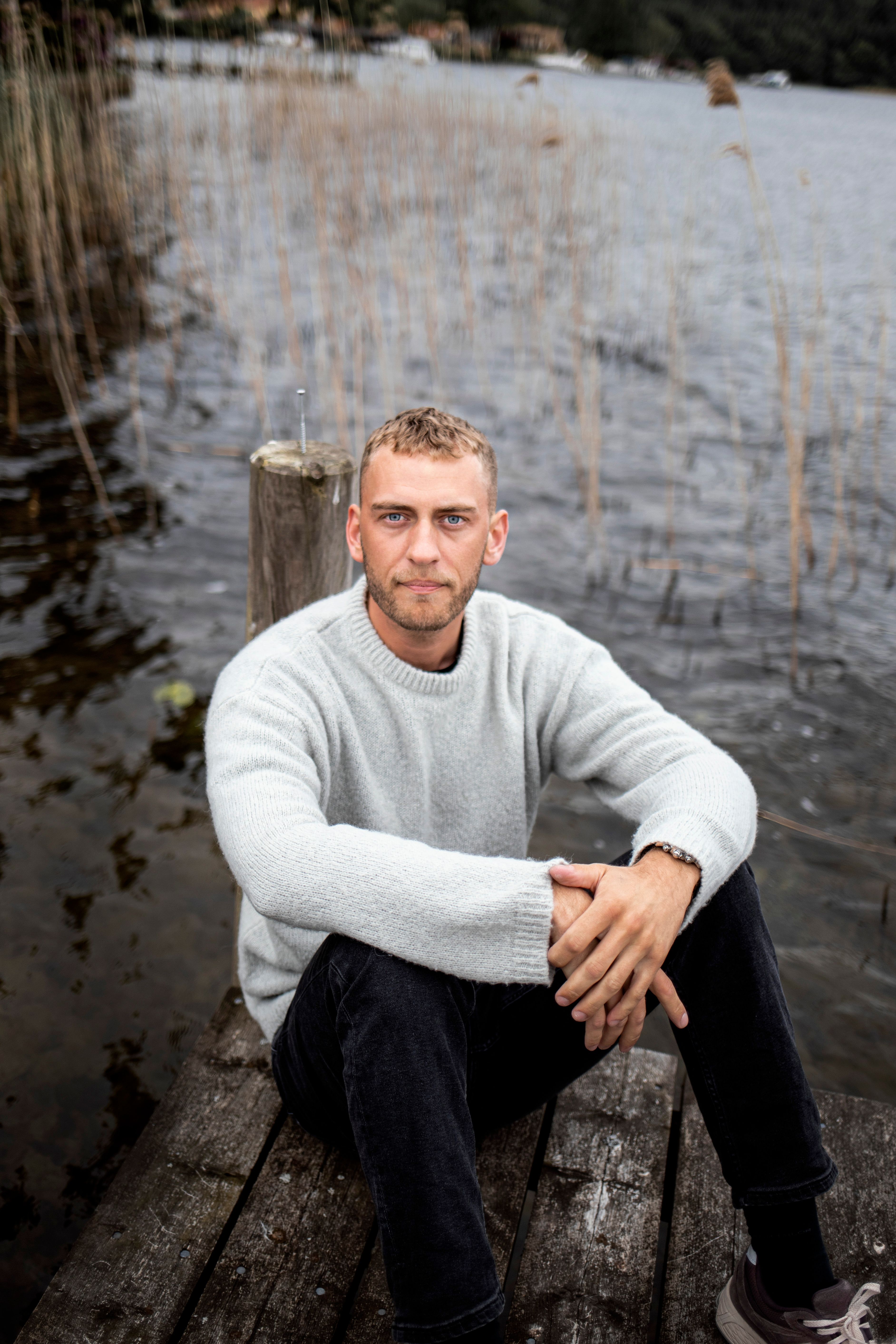A man sits on a wooden pier by Silkeborg Lake in Denmark, enjoying a leisurely moment.