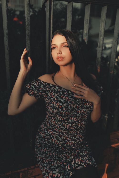 Free Stylish portrait of a woman in a floral dress posing by metal rails with dramatic lighting. Stock Photo