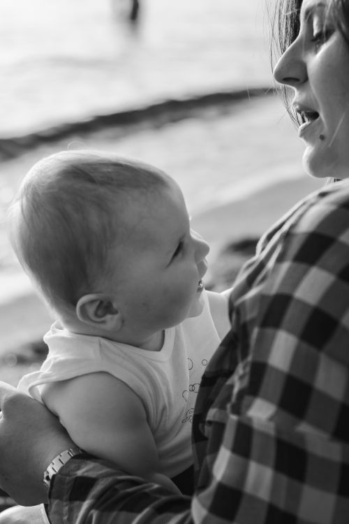 Free A black and white image capturing a tender moment between a mother and her baby by the seaside. Stock Photo