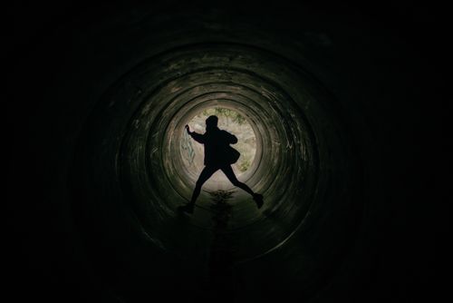 Free Silhouette of an active person jumping within a dark circular tunnel. Stock Photo