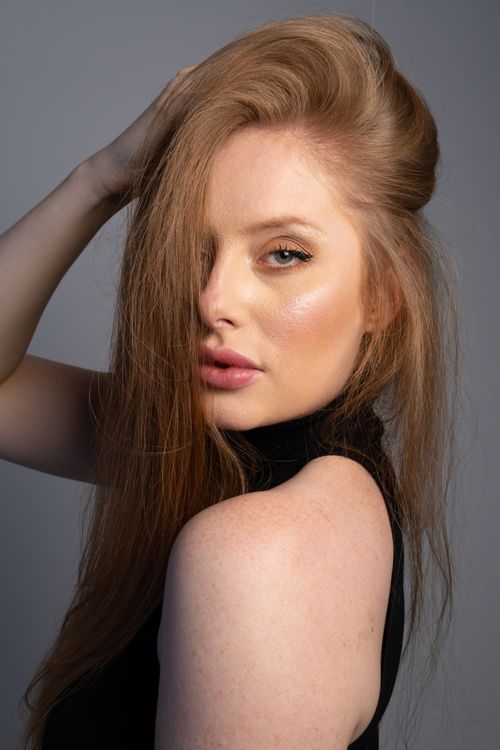 Free Striking portrait of a woman with long hair posing against a gray backdrop in a studio. Stock Photo