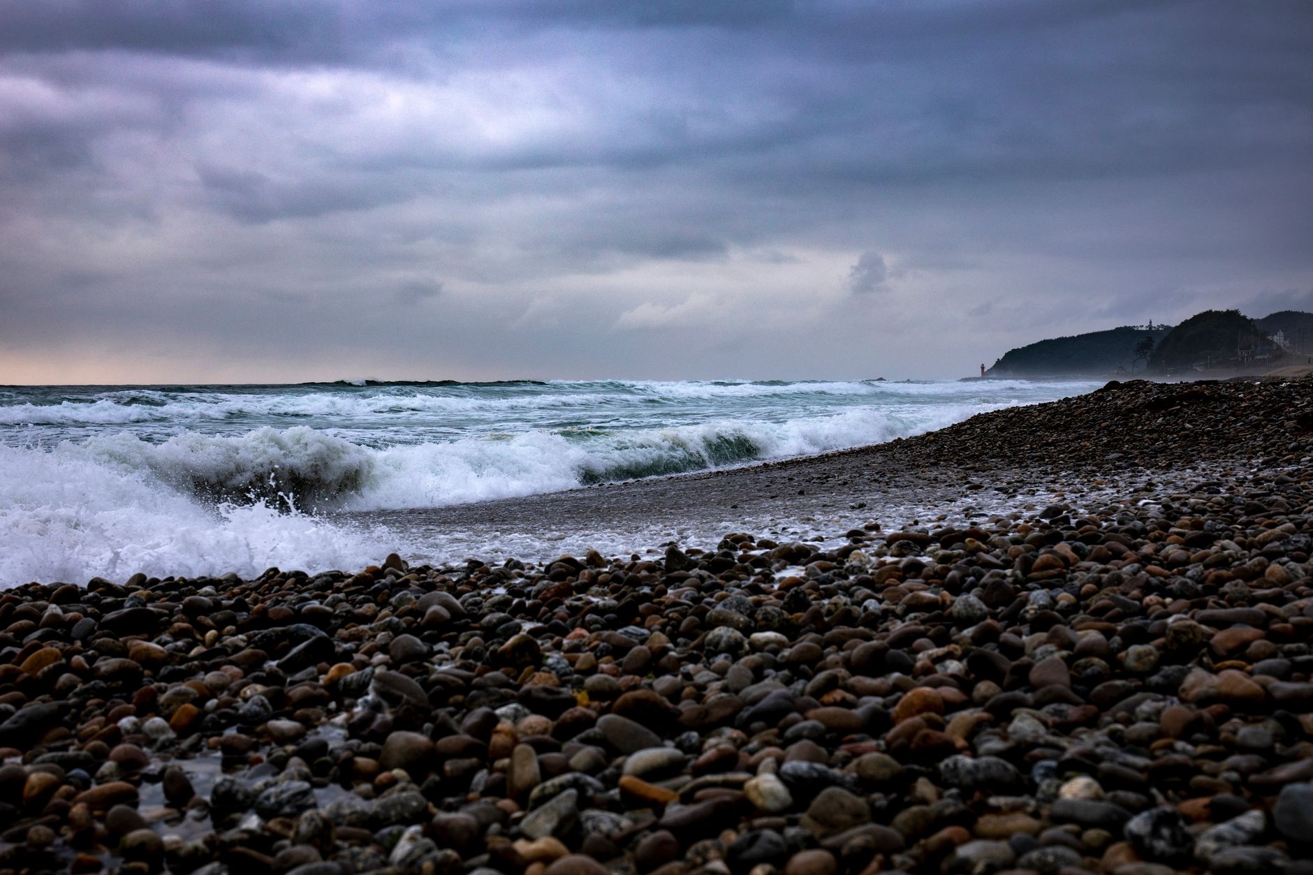 Dramatic waves crash on a rocky shore under a cloudy sky at Yangyang, South Korea.