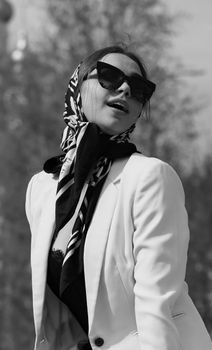 Elegant woman posing in a fashionable scarf and sunglasses, exuding vintage style.