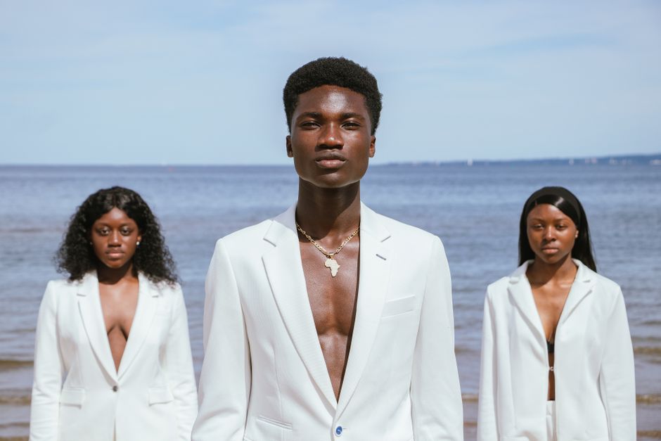 Three models in white blazers posing elegantly by the sea.