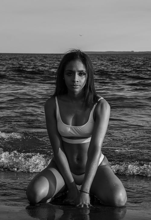 Grayscale Photo of a Woman in Bikini Sitting on the Beach