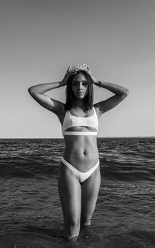 Elegant black and white portrait of a woman standing in the ocean wearing swimwear.