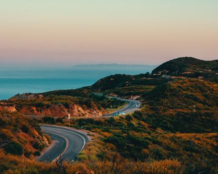 Stunning aerial view of a winding highway in Malibu with ocean and mountains at sunset.
