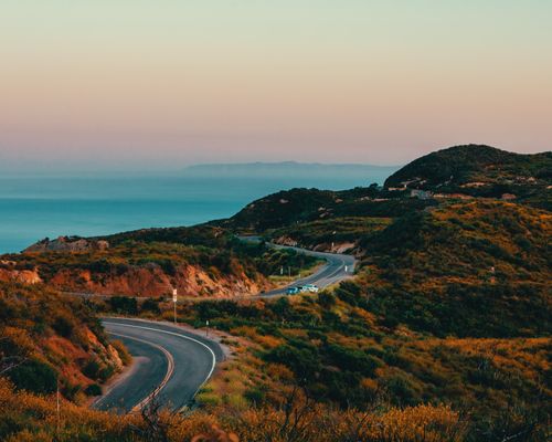Free Stunning aerial view of a winding highway in Malibu with ocean and mountains at sunset. Stock Photo