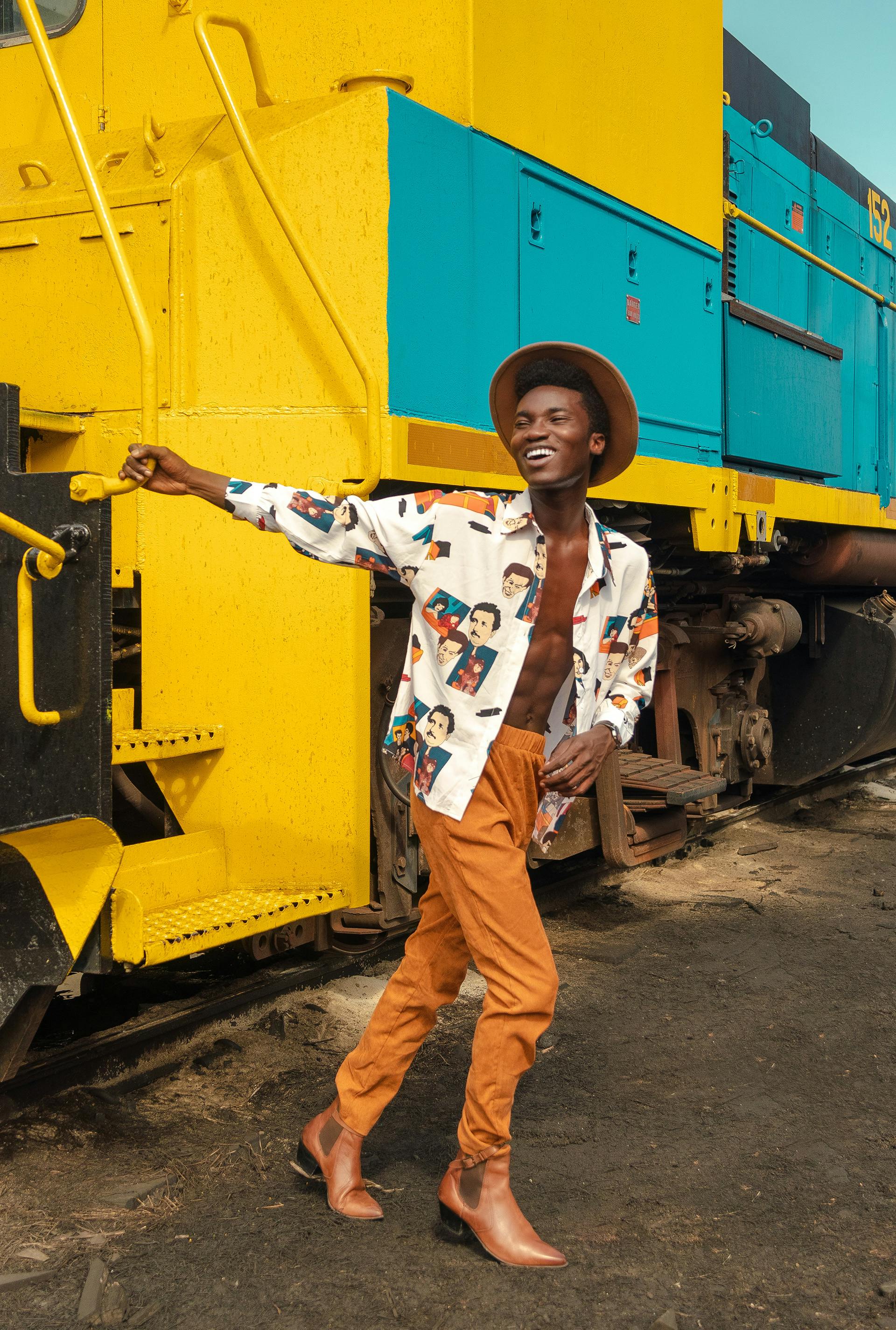 A fashionable man in vibrant attire posing confidently by a colorful train.