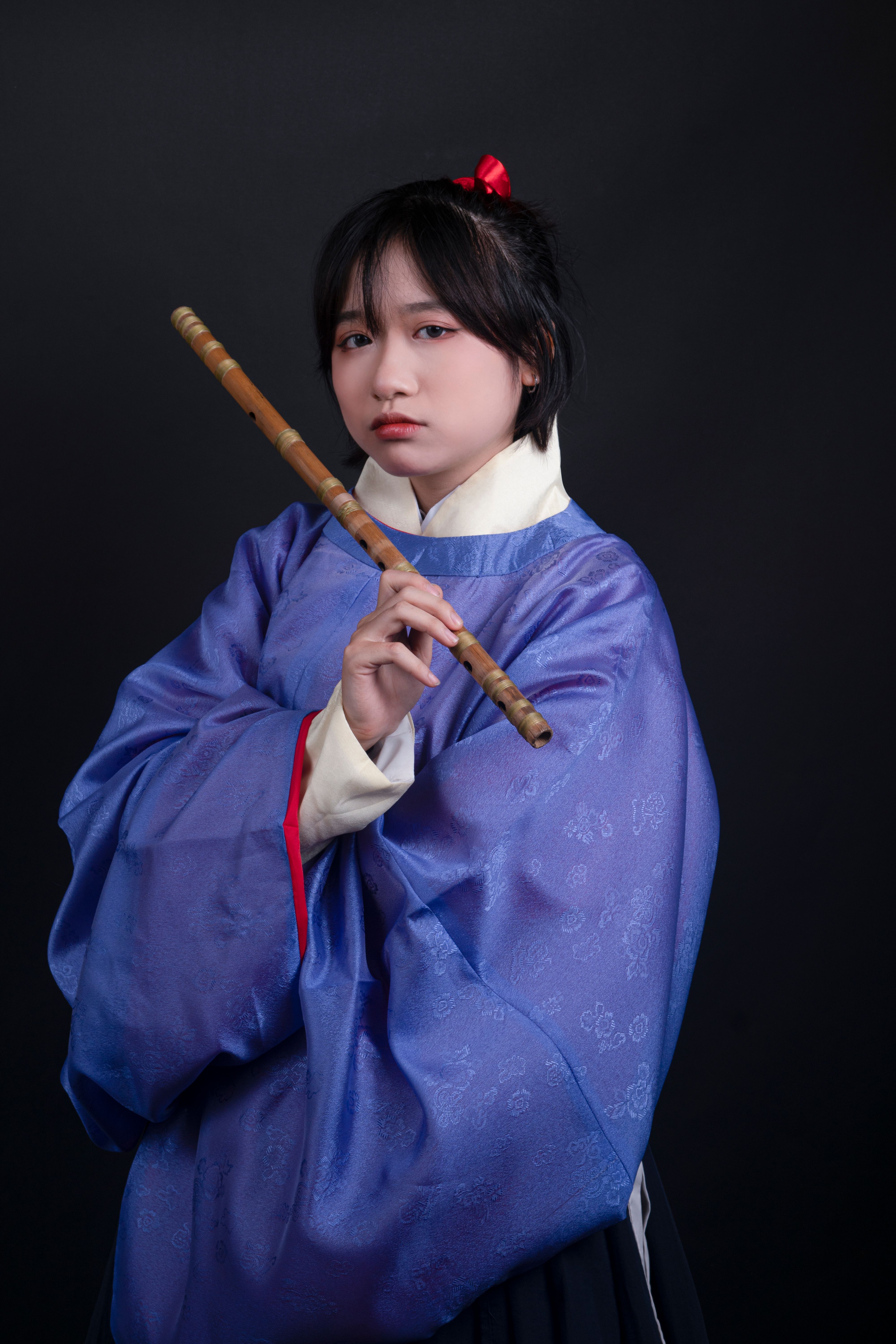 Portrait of a woman in traditional attire holding a flute in studio setting.