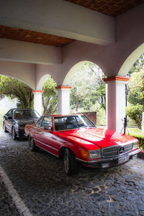 Free A classic red car parked under an elegant stone archway with lush greenery in the background. Stock Photo