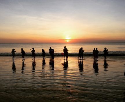 Silhouetted people enjoying a stunning sunset on a Bali beach.