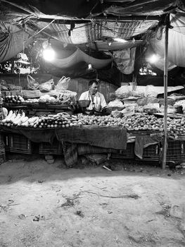 A busy market stall with a vendor selling fresh fruits and vegetables at night.