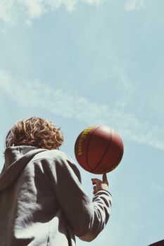 A person spins a basketball under a bright blue sky in a dynamic, low angle shot.