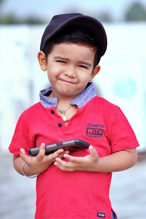 Cute Boy Smiling in Red Shirt Holding a Mobile Phone