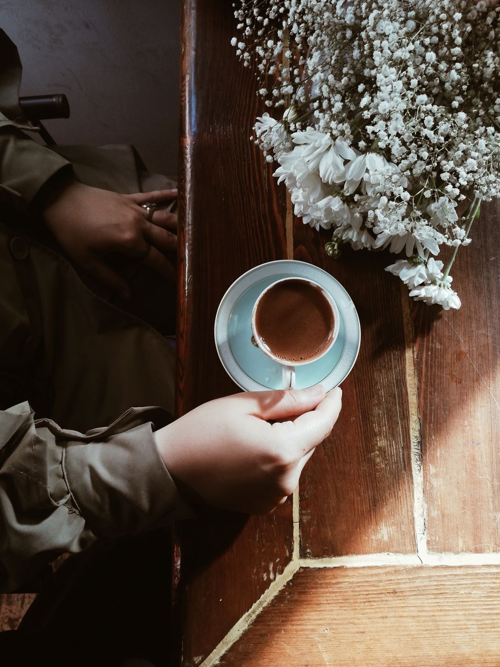 Atmospheric shot of a hand holding a coffee cup by a rustic table adorned with flowers.