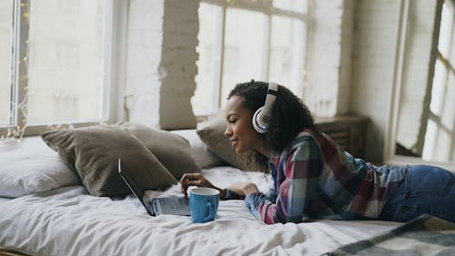 Smiling Girl in Headphones Relaxing on Bed with Laptop 