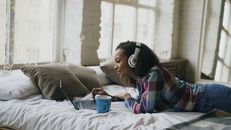 Smiling Girl in Headphones Relaxing on Bed with Laptop