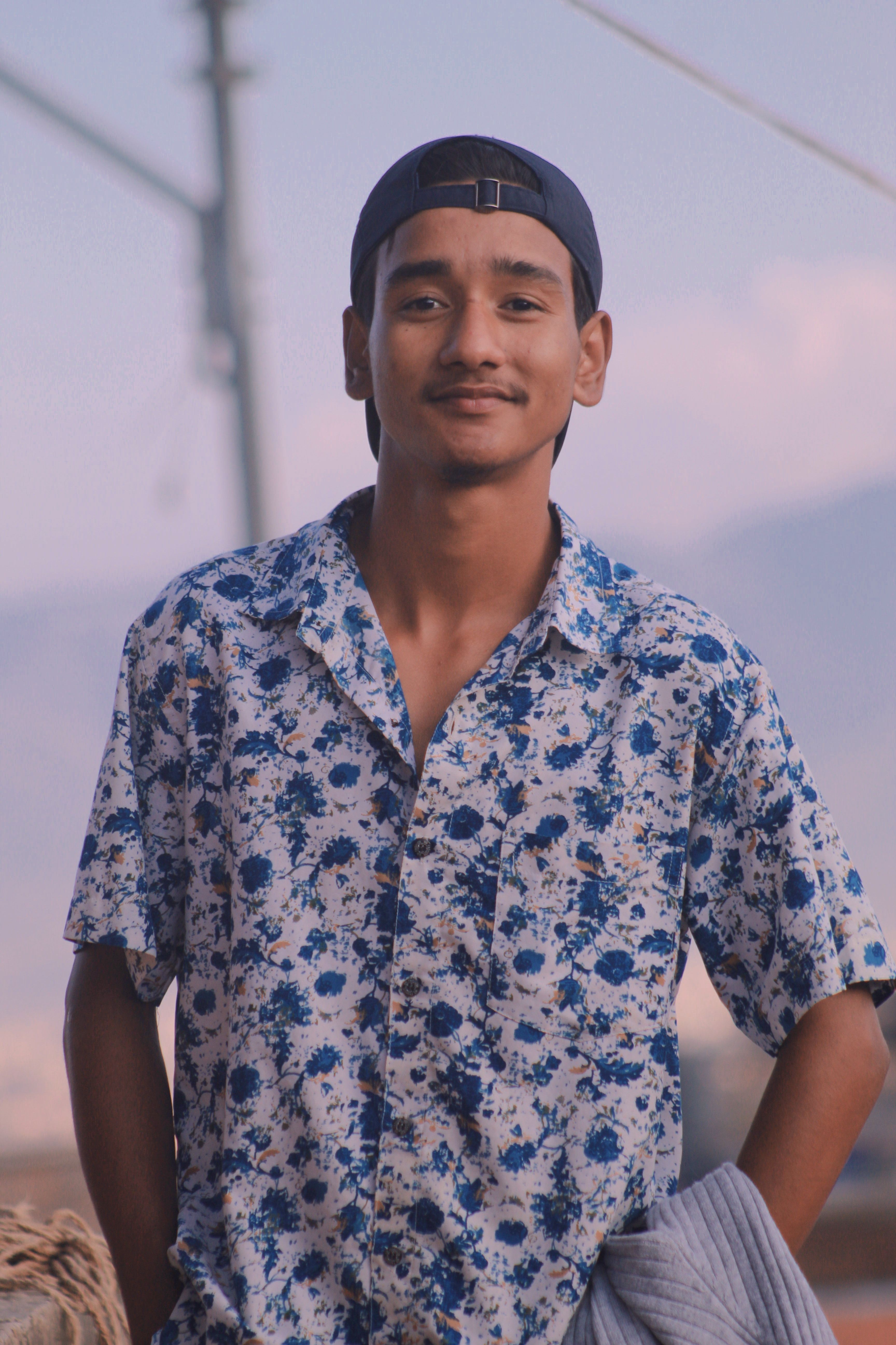 Portrait of a young man in a floral shirt smiling outdoors.