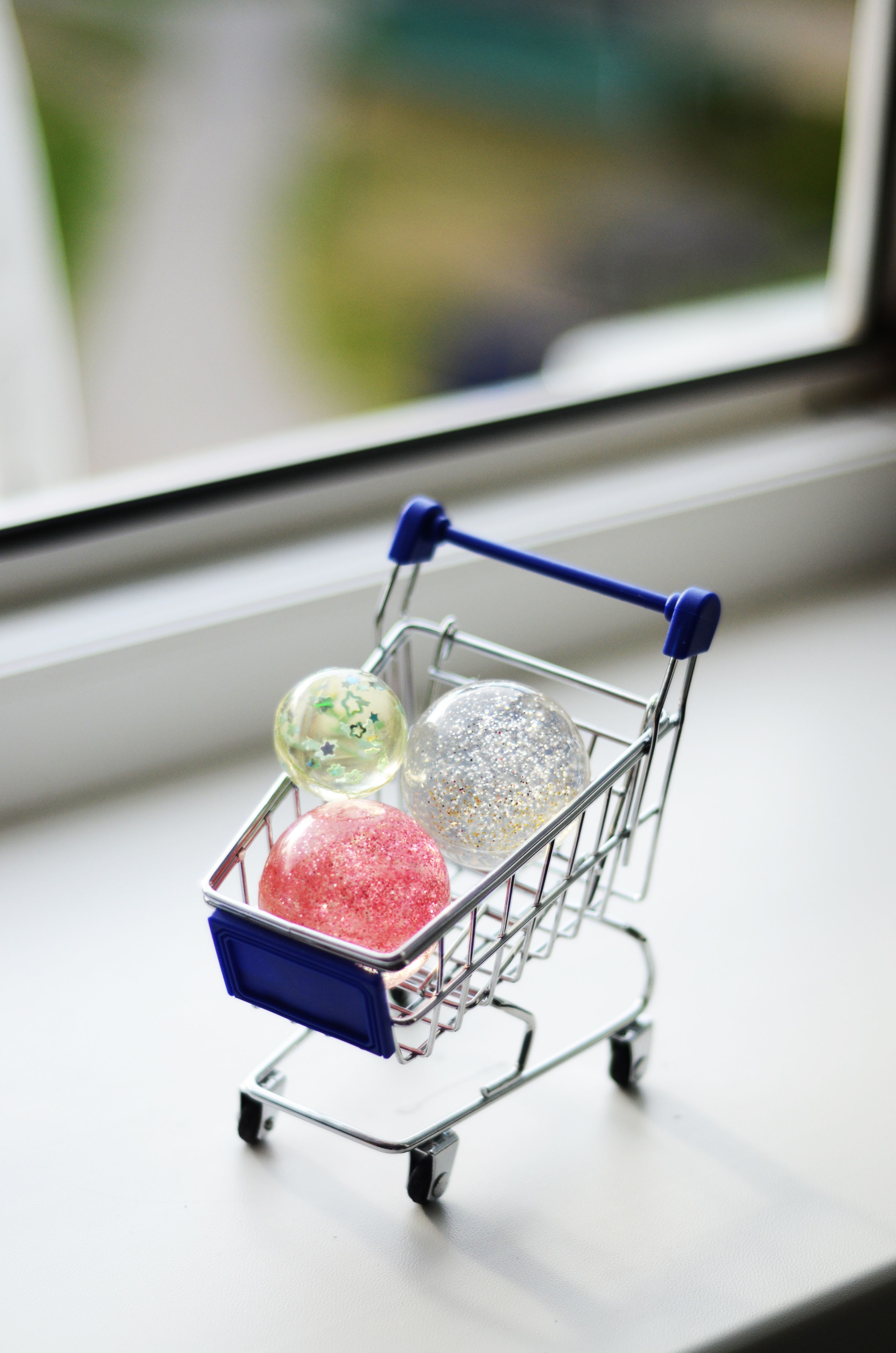 Miniature shopping cart holding colorful balls on a windowsill, perfect for a playful concept.