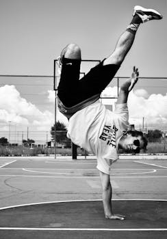 Energetic dancer performs a handstand on a basketball court, showcasing athletic street dance moves.
