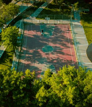 An aerial shot of a basketball court surrounded by greenery, featuring a lone player.