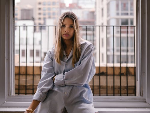 Woman in White and Blue Striped Long Sleeves Sitting on the Window Sill 